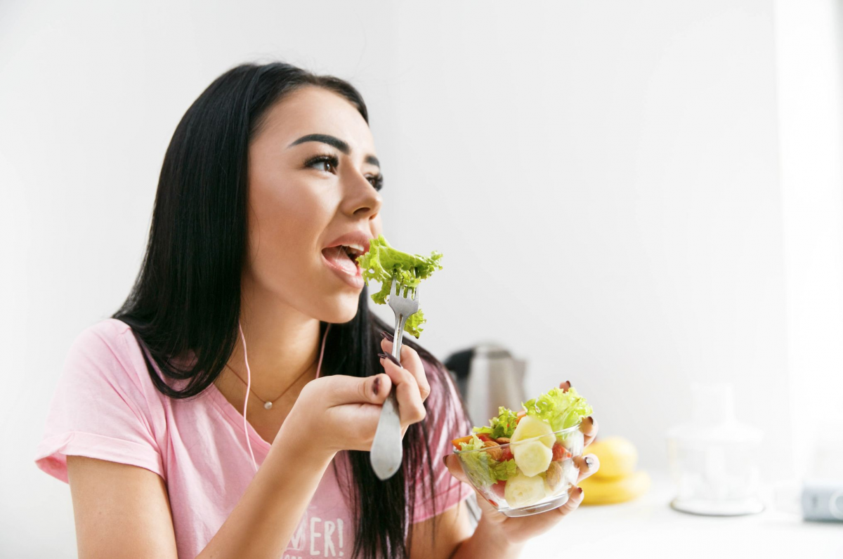 Seorang wanita sedang makan sayur dan buah-buahan